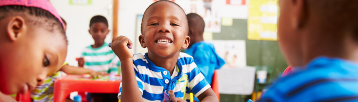 A young boy smiles to the camera while sitting in a table with other ECE students.